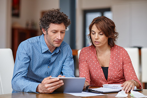 Comparing student loans. A man and woman sit next to each other looking at papers and a tablet the man is holding.